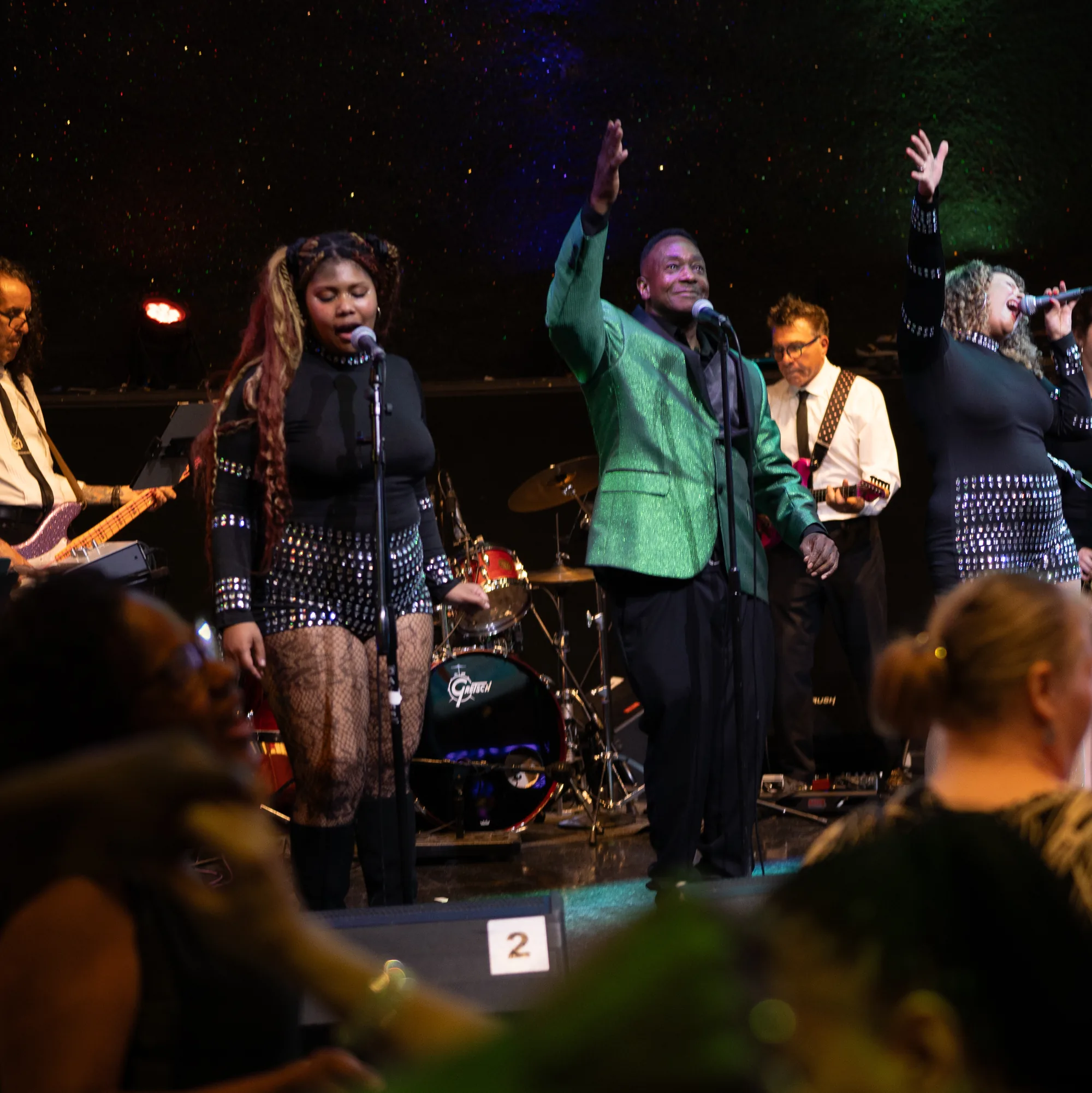 Spotlite's vocalists onstage with hands raised as guests dance in front of the stage